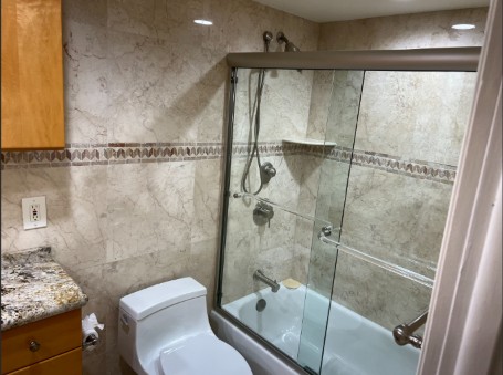 Condo bathroom with a glass-enclosed tub, tiled walls and granite vanity